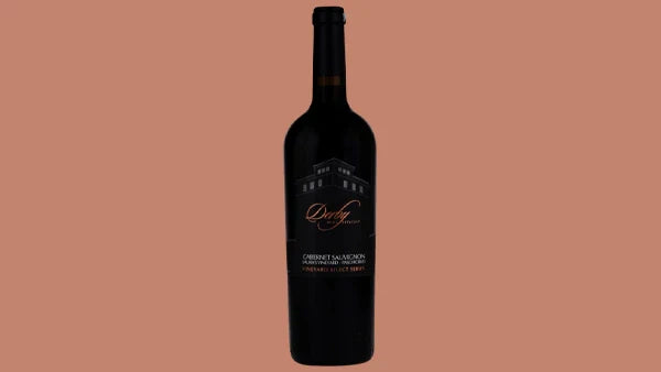 Bottle of Derby Cabernet Sauvignon with a dark label in script lettering, on a salmon background