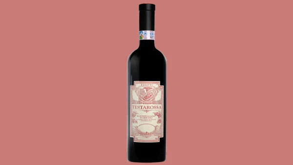 Bottle of Testarossa red wine with an ornate cream and pink label, on a pink background