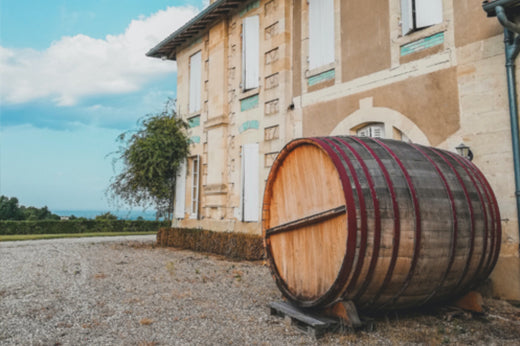 Large oak wine barrel on gravel outside a shuttered stone chateau in Bordeaux