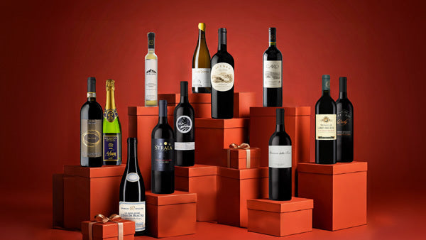 Wine bottles arranged on stacked red gift boxes against a deep red background
