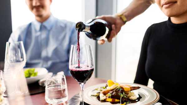 waiter serving red wine for female customer at restaurant