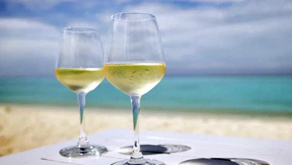 Two glasses of white wine on a table overlooking a sandy beach and turquoise sea