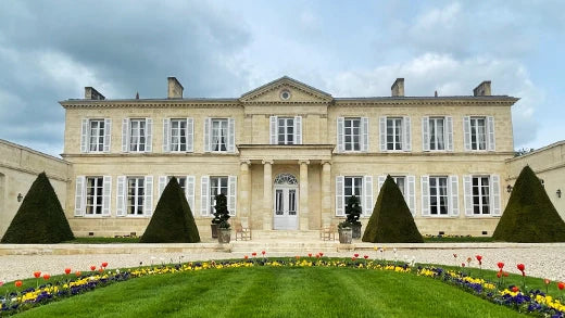Symmetrical stone chateau with shuttered windows, clipped topiary cones and tulip beds in front