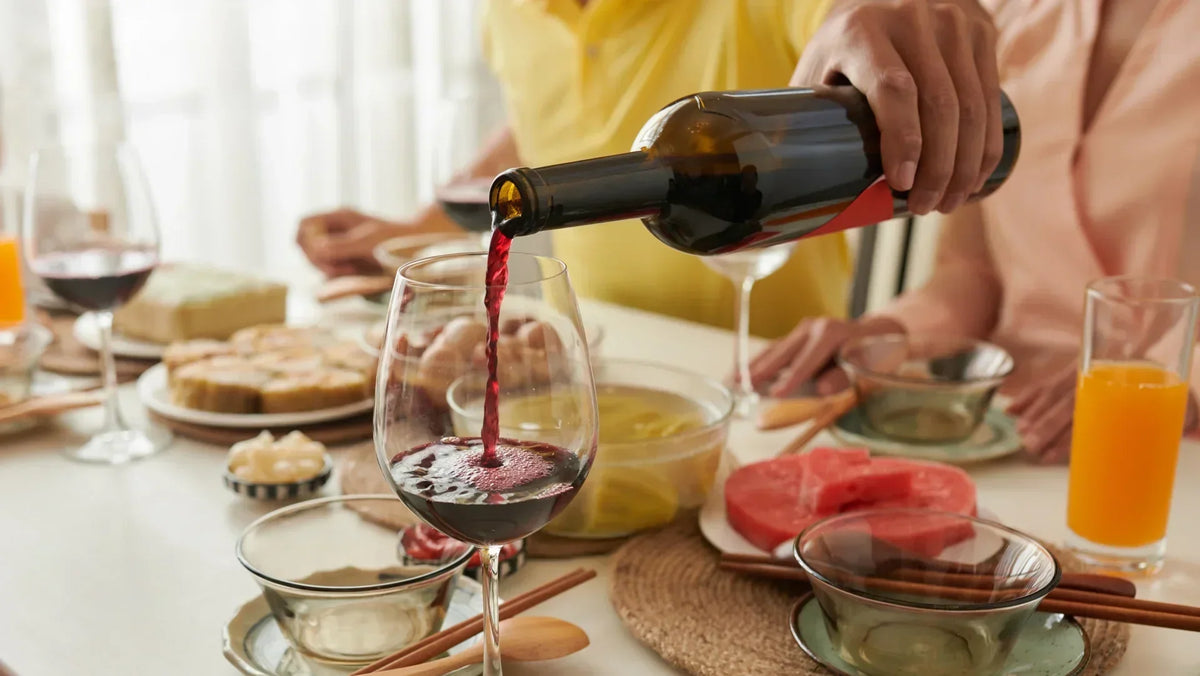 Red wine poured into a glass at a breakfast table set with bread, fruit and orange juice