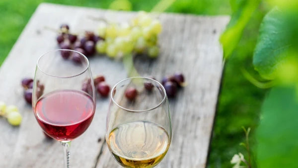 Glass of rose and glass of white wine on a weathered wooden table with red and green grapes