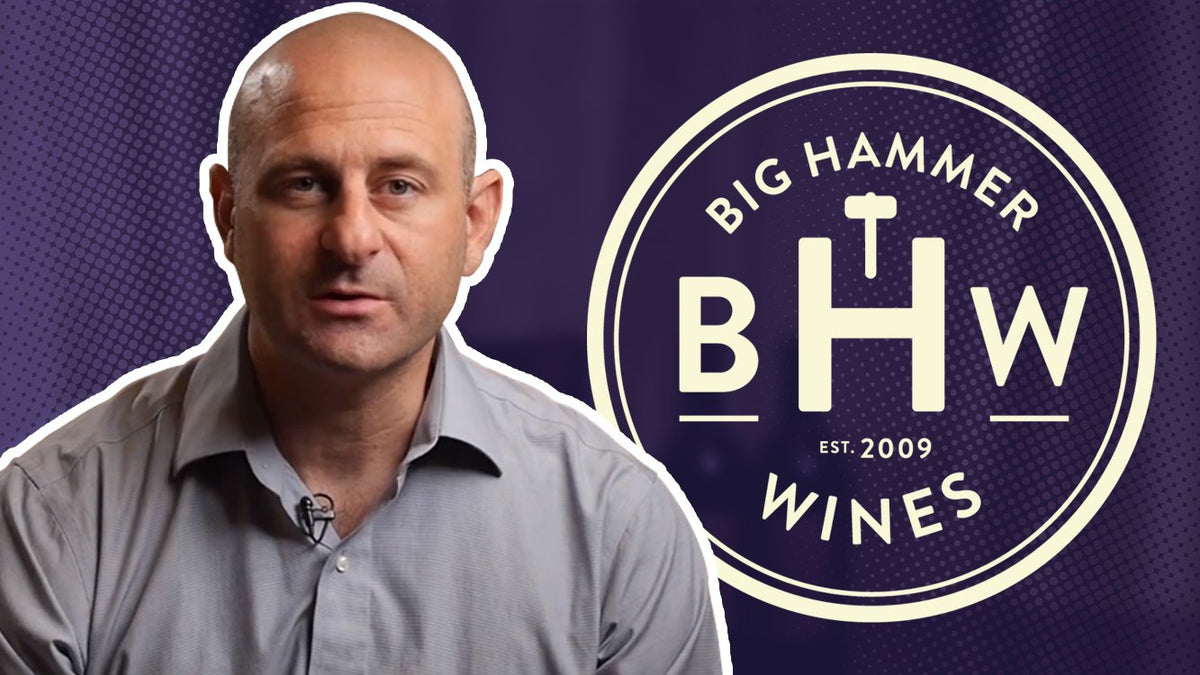 Man speaking to camera beside the Big Hammer Wines logo on a purple background