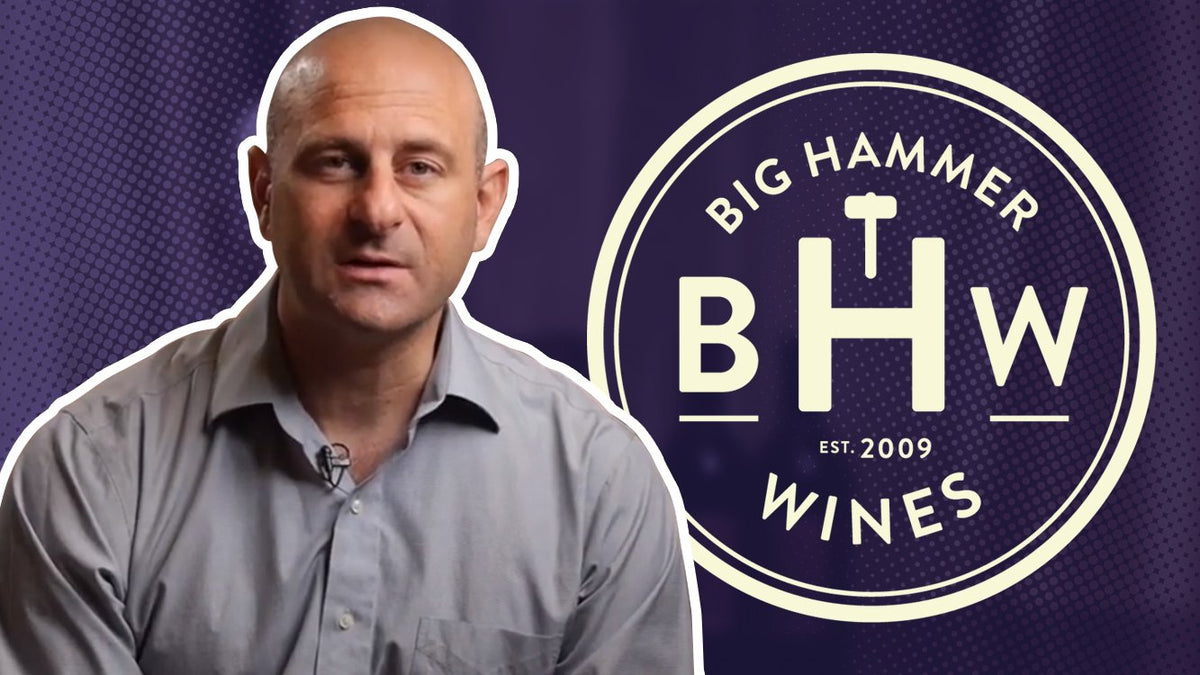 Man in a grey shirt speaking to camera beside the Big Hammer Wines logo