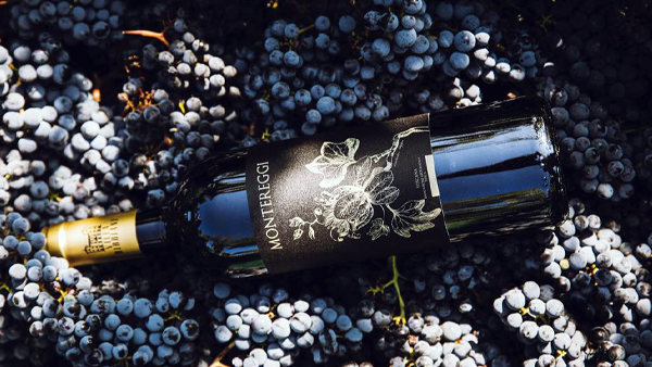 Bottle of Monteraggi wine lying on a bed of dark grapes, label with etched floral design
