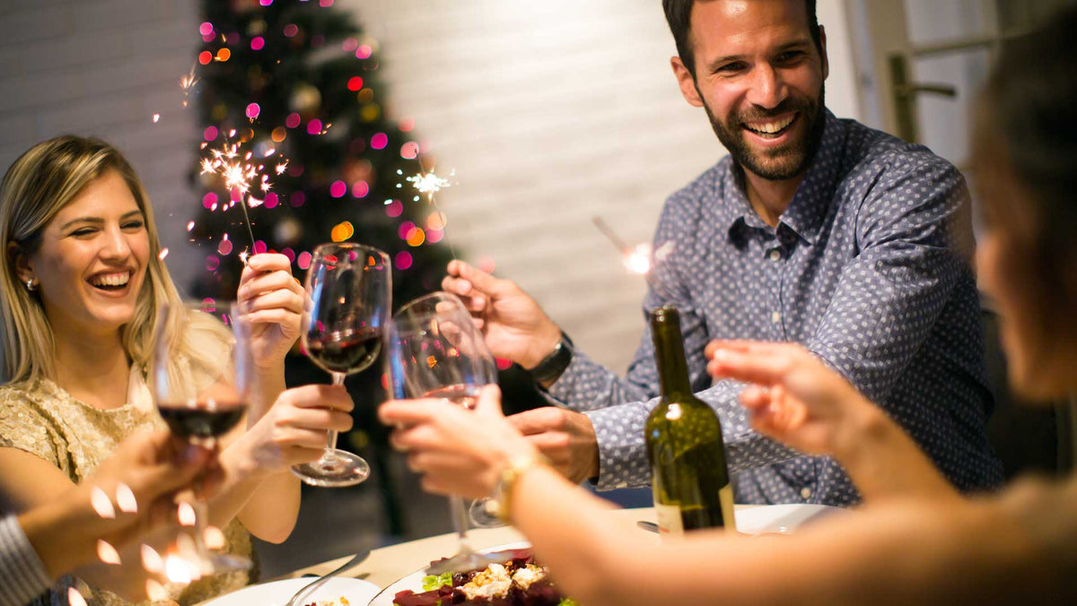 Friends toasting glasses of red wine with sparklers beside a lit Christmas tree