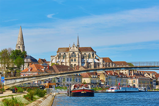 Riverside town in Burgundy with a Gothic abbey, a bridge and boats moored along the river