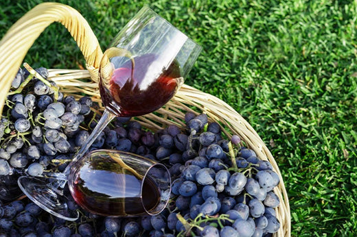 Wicker basket of dark grapes on grass with two tilted glasses of red wine