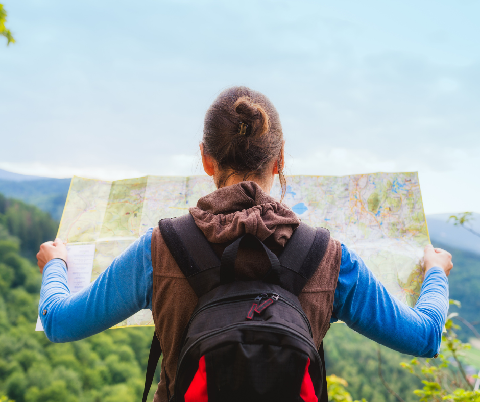 Hiker with a backpack seen from behind holding an open map above forested hills