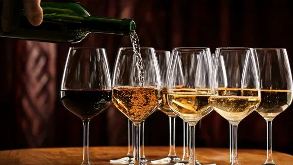 Sparkling wine poured from a green bottle into a row of glasses on a wooden table