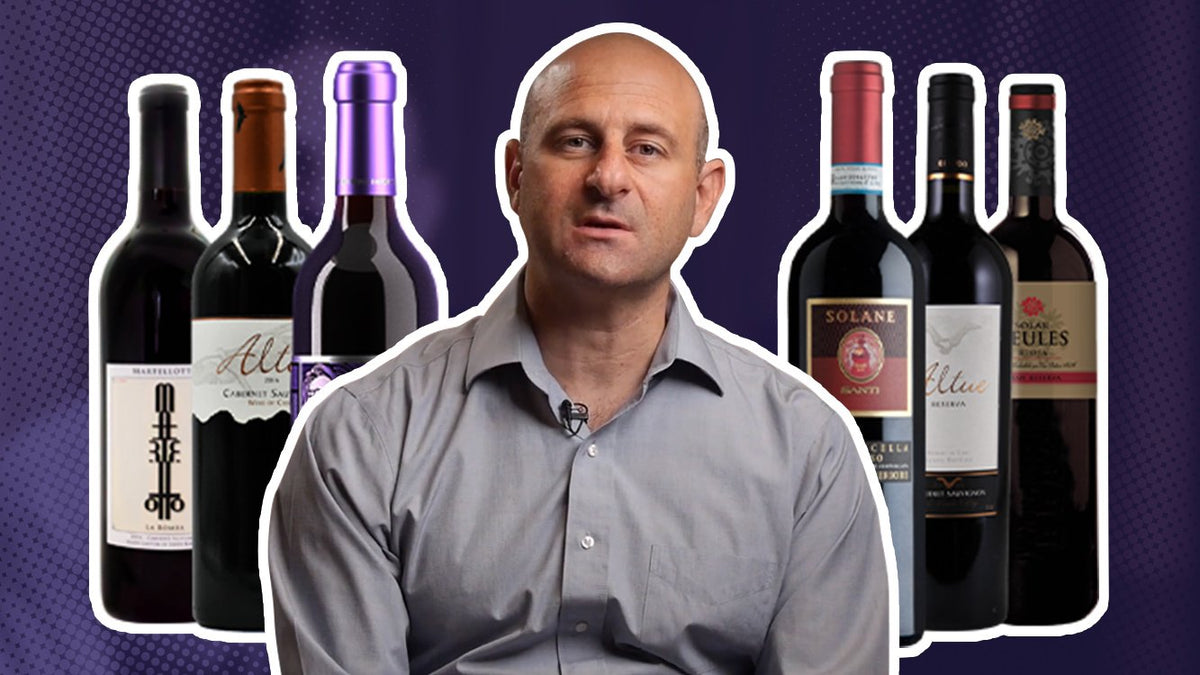 Man in a grey shirt with six bottles of red wine arranged around him