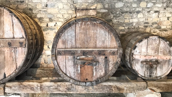 Three large wooden wine barrels resting on a rack against a stone cellar wall