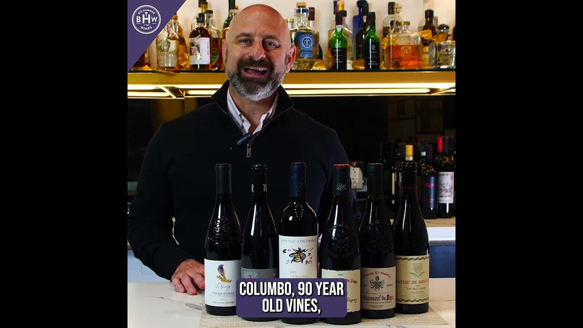 Man behind a bar with six red wine bottles, caption reading "Columbo, 90 year old vines"