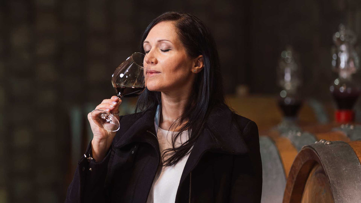 Woman in a dark coat nosing a glass of red wine in a barrel cellar