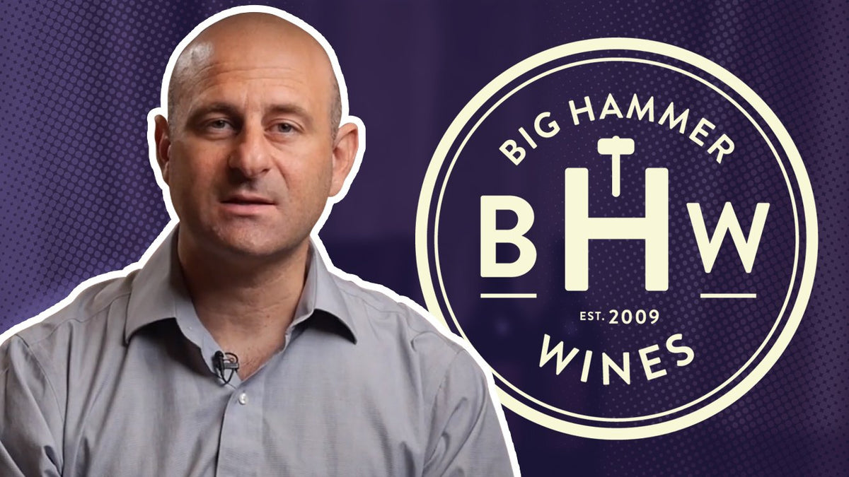 Man wearing a clip-on microphone and grey shirt beside the Big Hammer Wines logo