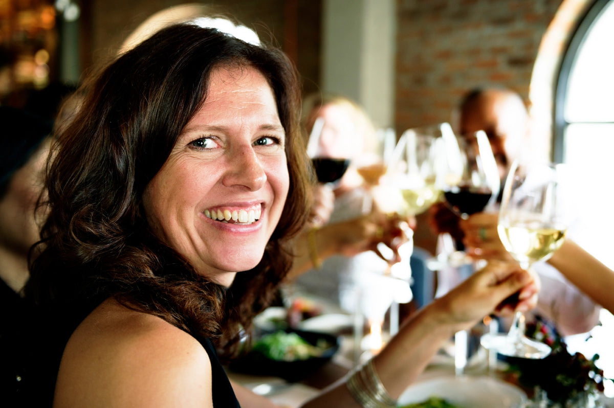 Smiling woman at a dinner table as others raise glasses of red and white wine