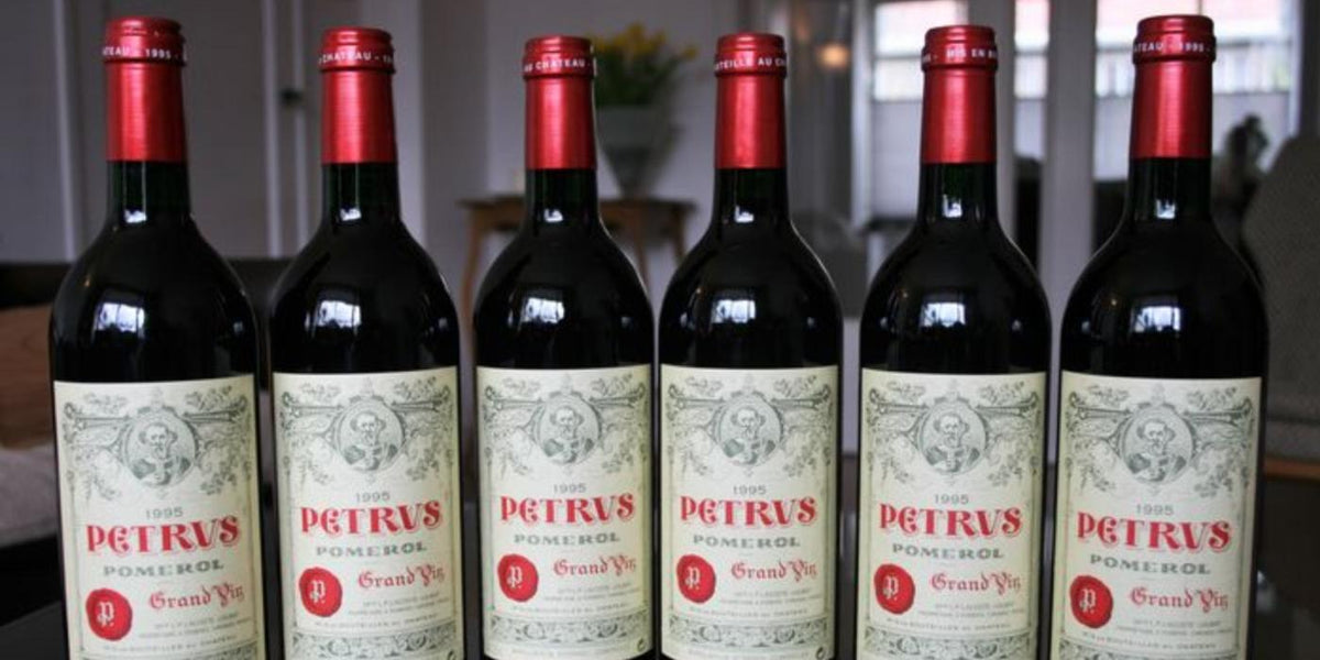 Six bottles of Petrus Pomerol lined up, cream labels with red capsules