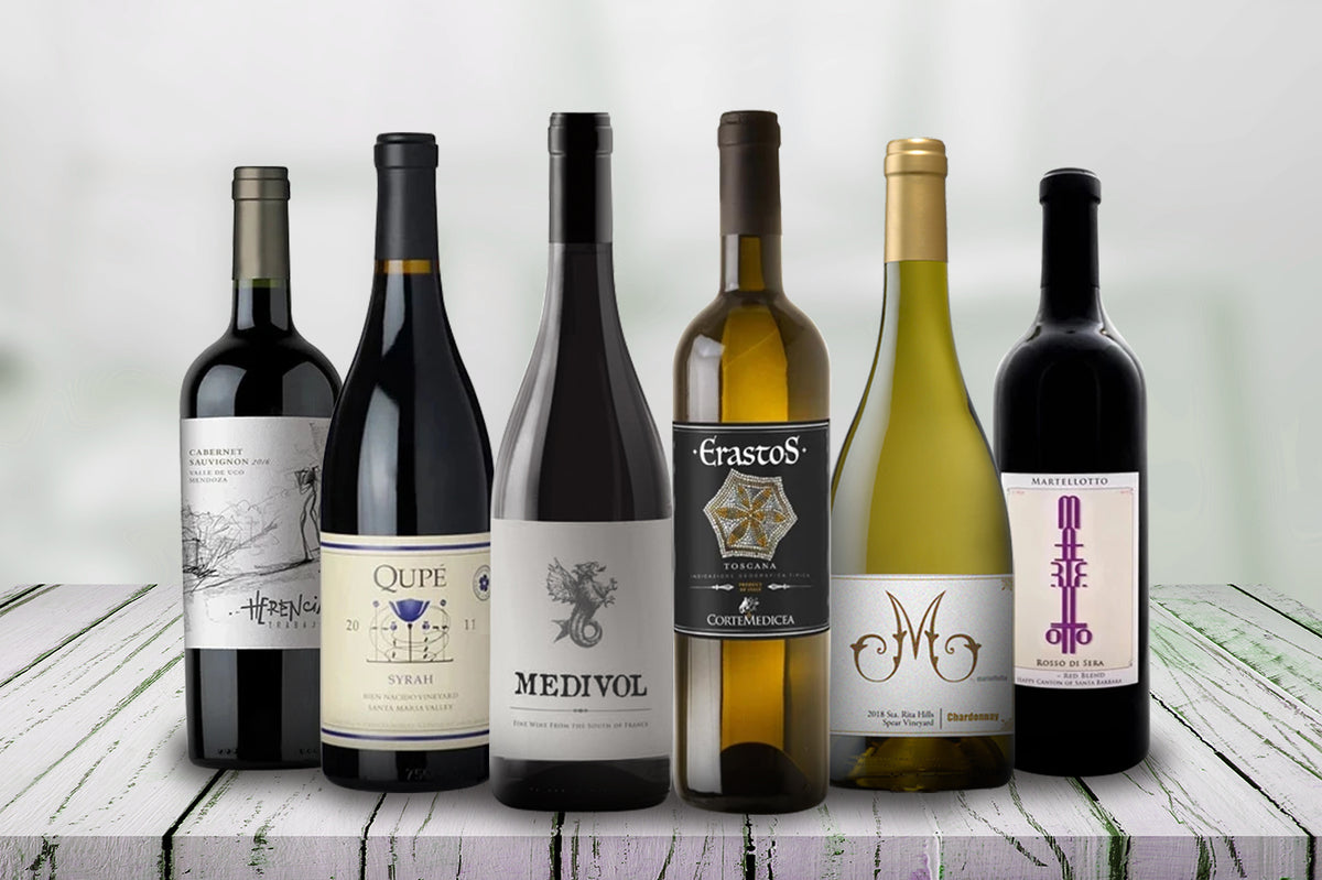 Six bottles of red and white wine standing on white wooden planks