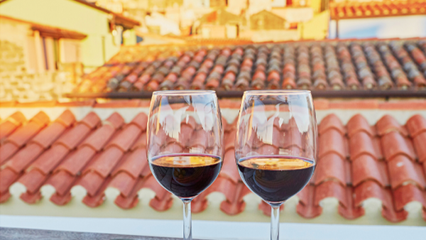 Two glasses of red wine on a ledge overlooking terracotta tile rooftops