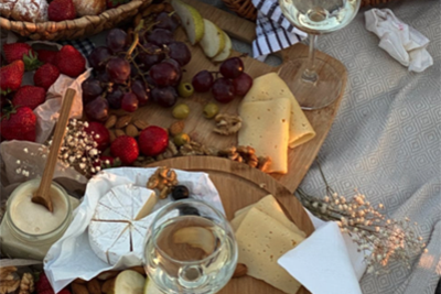Picnic cheese board with brie, grapes, strawberries, nuts and honey beside two glasses of white wine