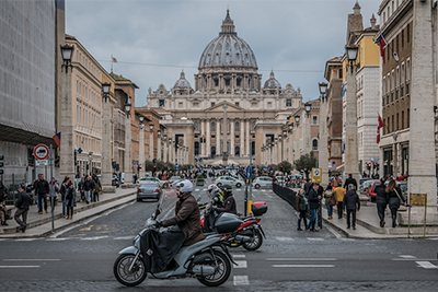 Scooter rider on a street leading to St. Peter's Basilica in Rome, with traffic and pedestrians