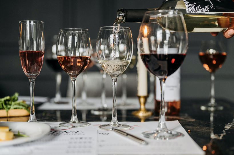 Red wine poured from a bottle into a glass beside flutes and glasses of sparkling, rose and white wine