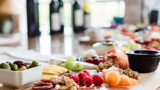 Close-up of a grazing board with olives, cheese, salami, berries and nuts, wine bottles blurred behind