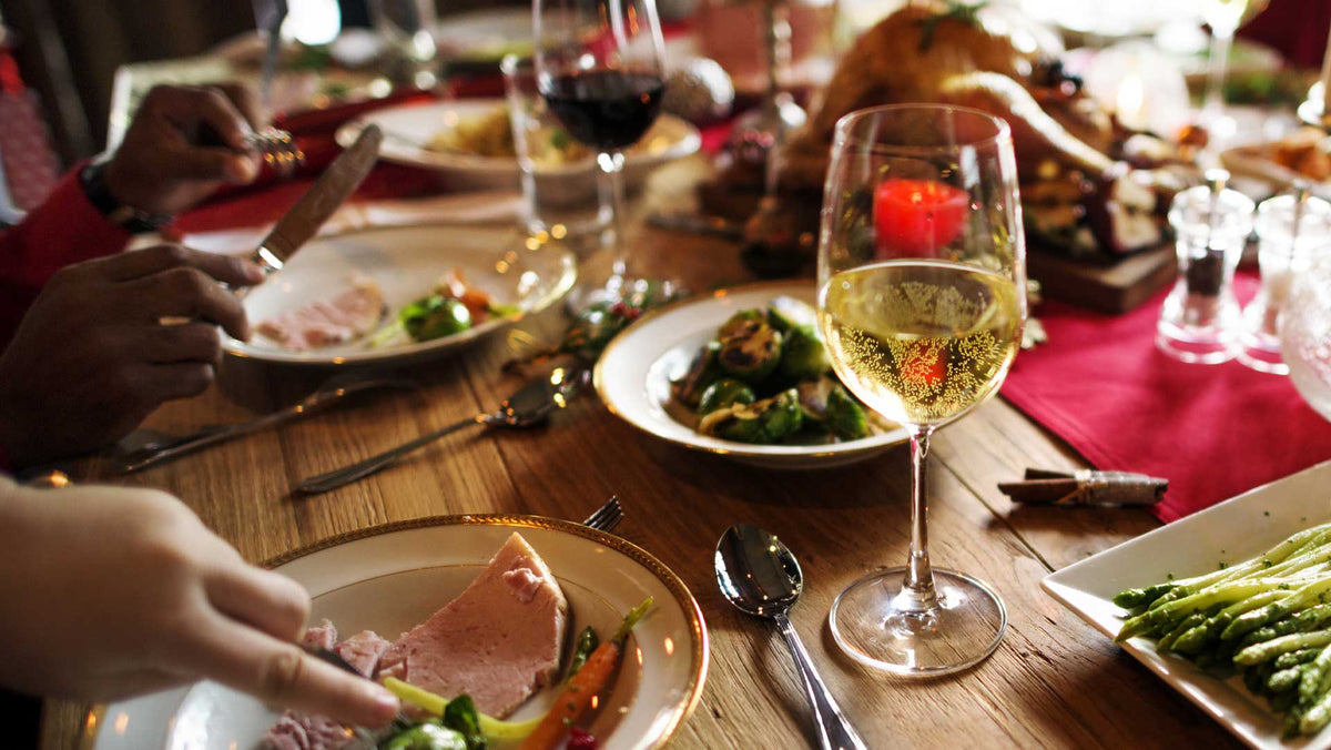 Festive dinner table with a glass of white wine, red runner, candles and plates being served