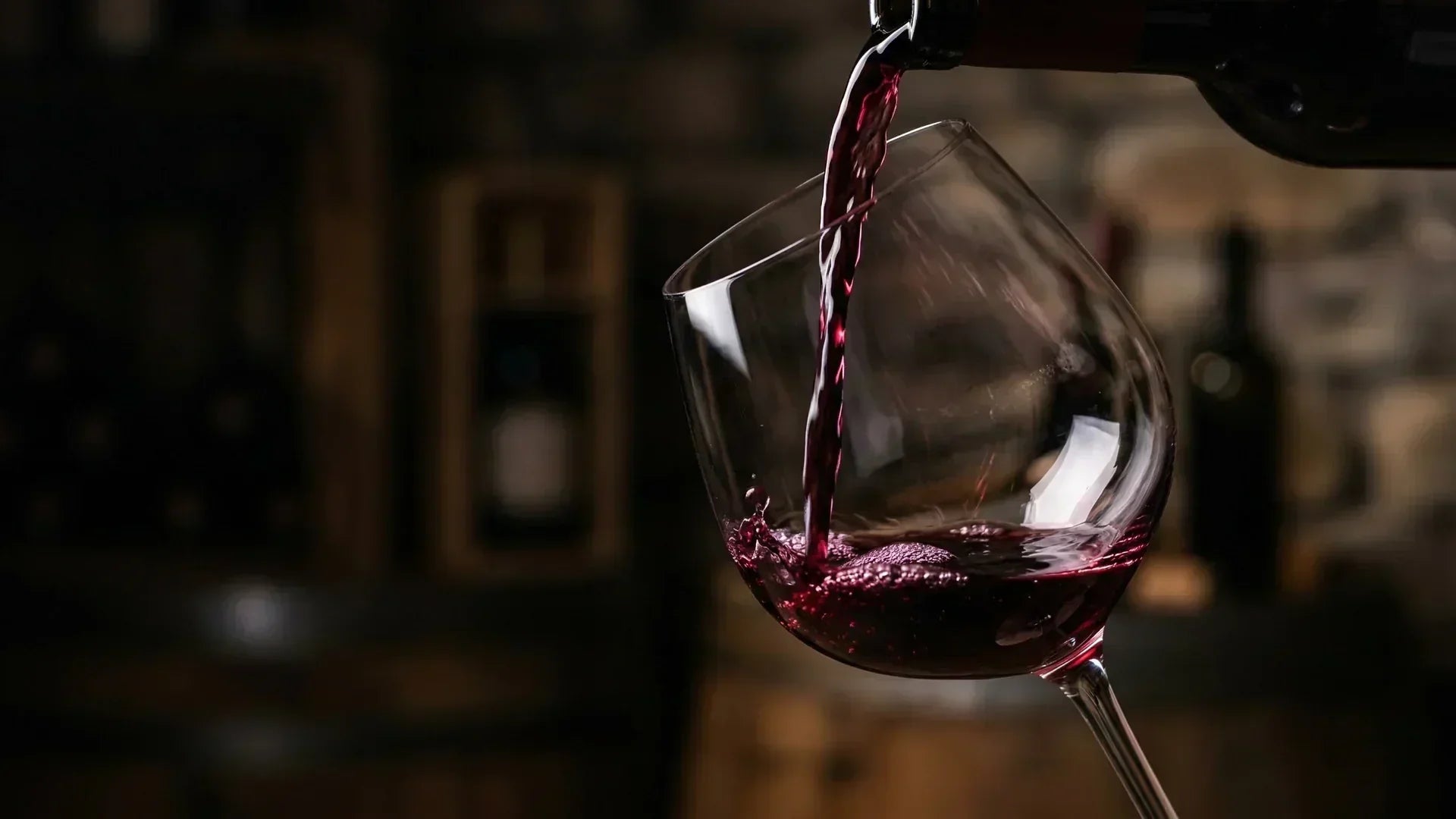 Red wine being poured into glass with dark background and soft lighting.
