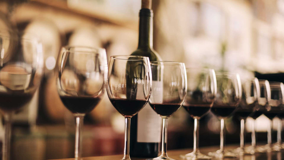 Row of glasses of red wine on a bar counter with a dark bottle behind them