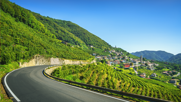 Winding road through steep vineyard-covered hills with a hillside village and church tower