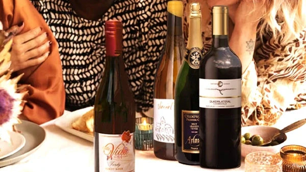 Four wine bottles on a candlelit dinner table: two reds, a white and a Champagne