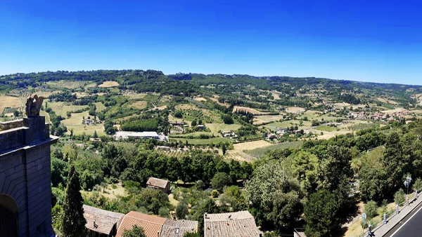 View from a hilltop stone wall over green countryside, farmland and rooftops under a clear blue sky