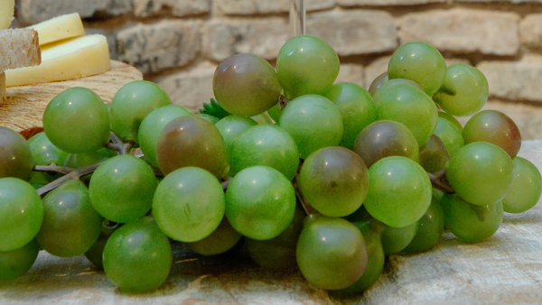 Close-up bunch of green grapes on a stone surface with wedges of cheese behind