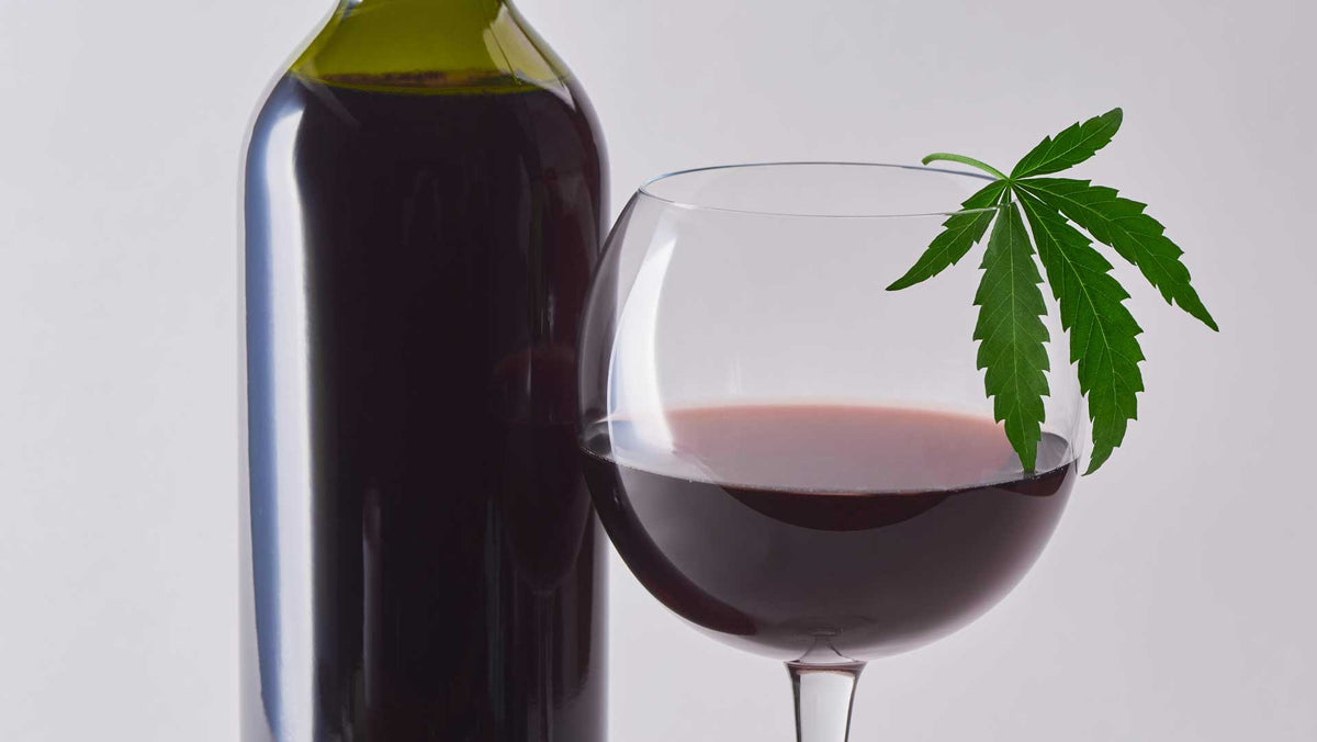 Glass of red wine with a cannabis leaf resting on the rim beside a dark wine bottle
