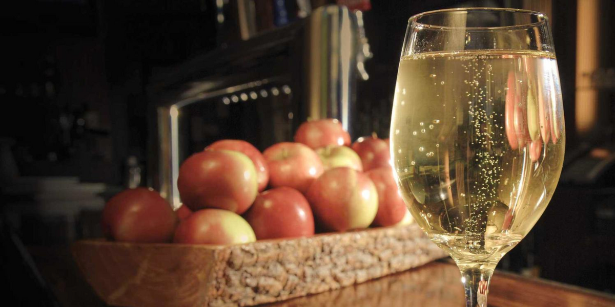 Glass of white wine beside a wooden crate of red apples near a fireplace