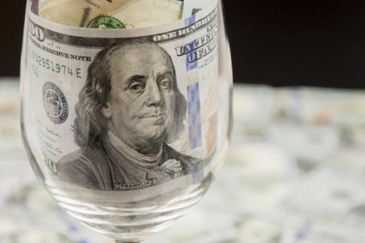 Empty wine glass in front of a hundred-dollar bill, Benjamin Franklin visible through the bowl