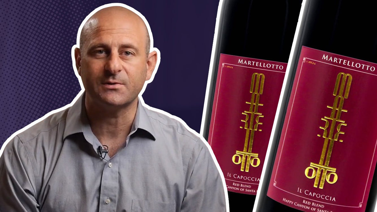 Man in a grey shirt beside two bottles of Martellotto Il Cappoccia red blend