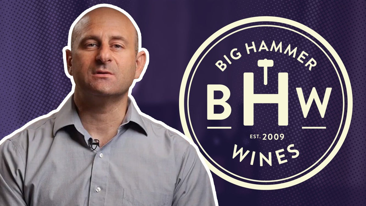 Man in a grey shirt looking at the camera with the Big Hammer Wines logo to his right