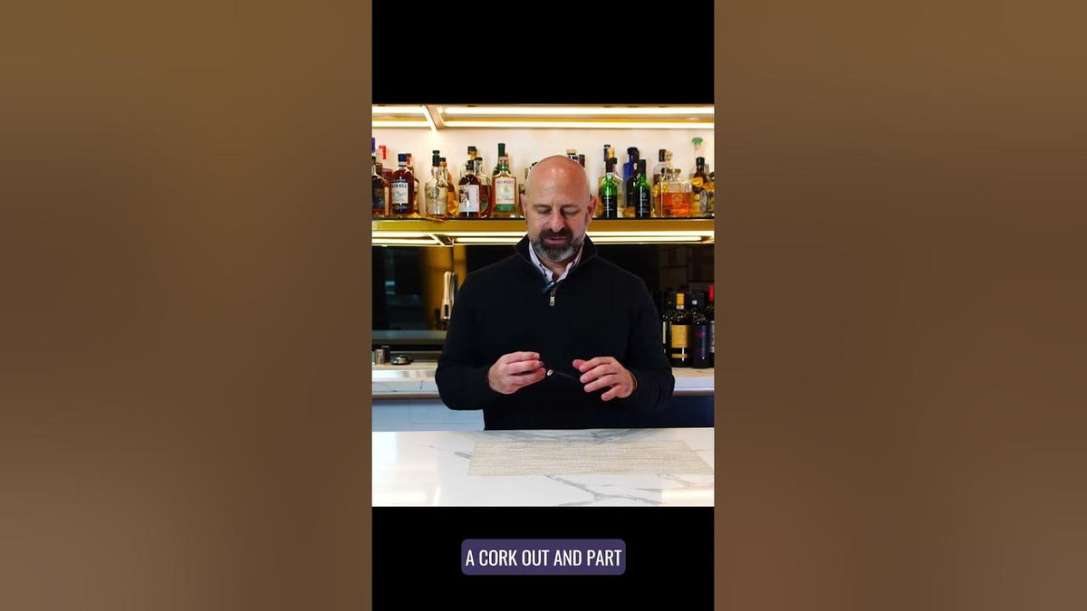 Man at a bar counter working a corkscrew, on-screen caption reading "A cork out and part"
