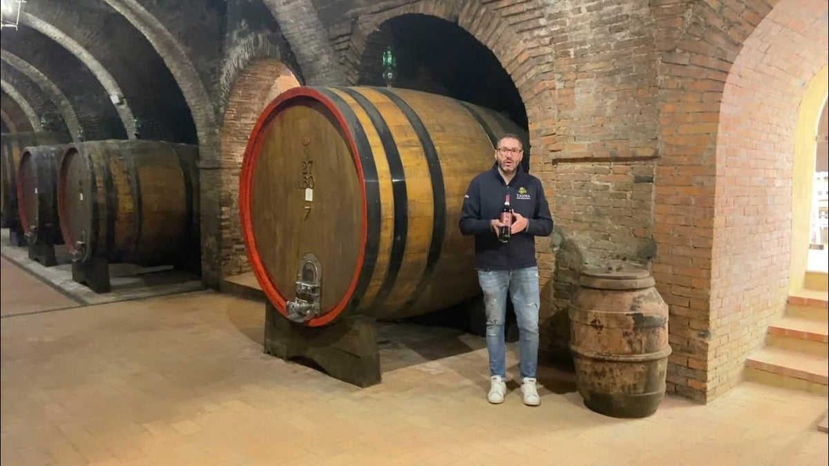 Man standing beside a large oval oak cask in a vaulted brick wine cellar