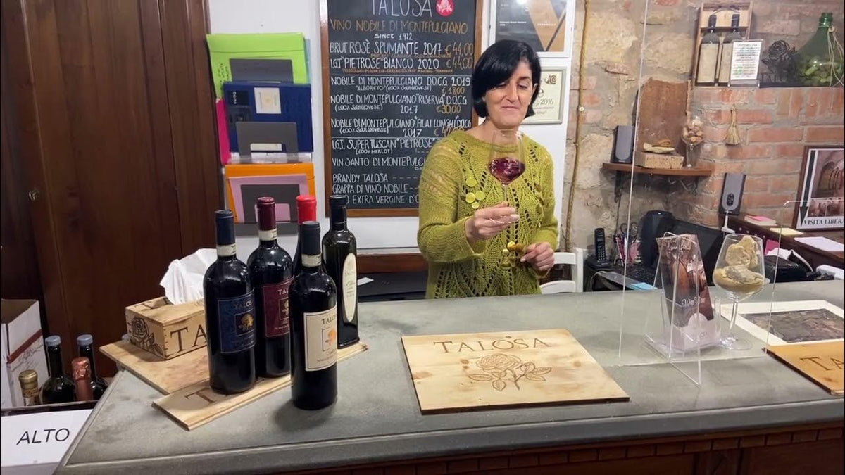 Woman swirling a glass of red wine at a Talosa tasting counter with bottles and a branded wooden crate
