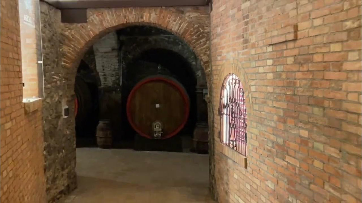 Brick archway in a wine cellar leading to a large round wooden cask