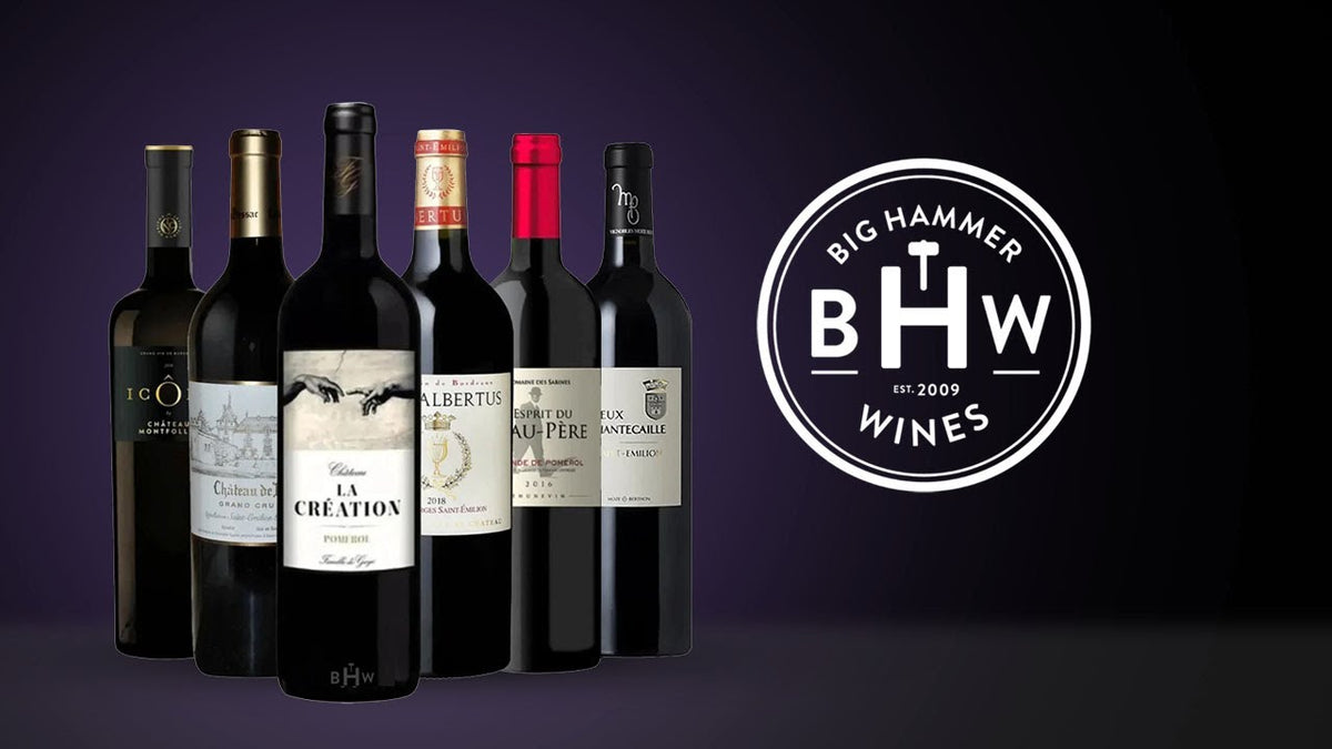 Six red wine bottles lined up beside the Big Hammer Wines logo on a purple background
