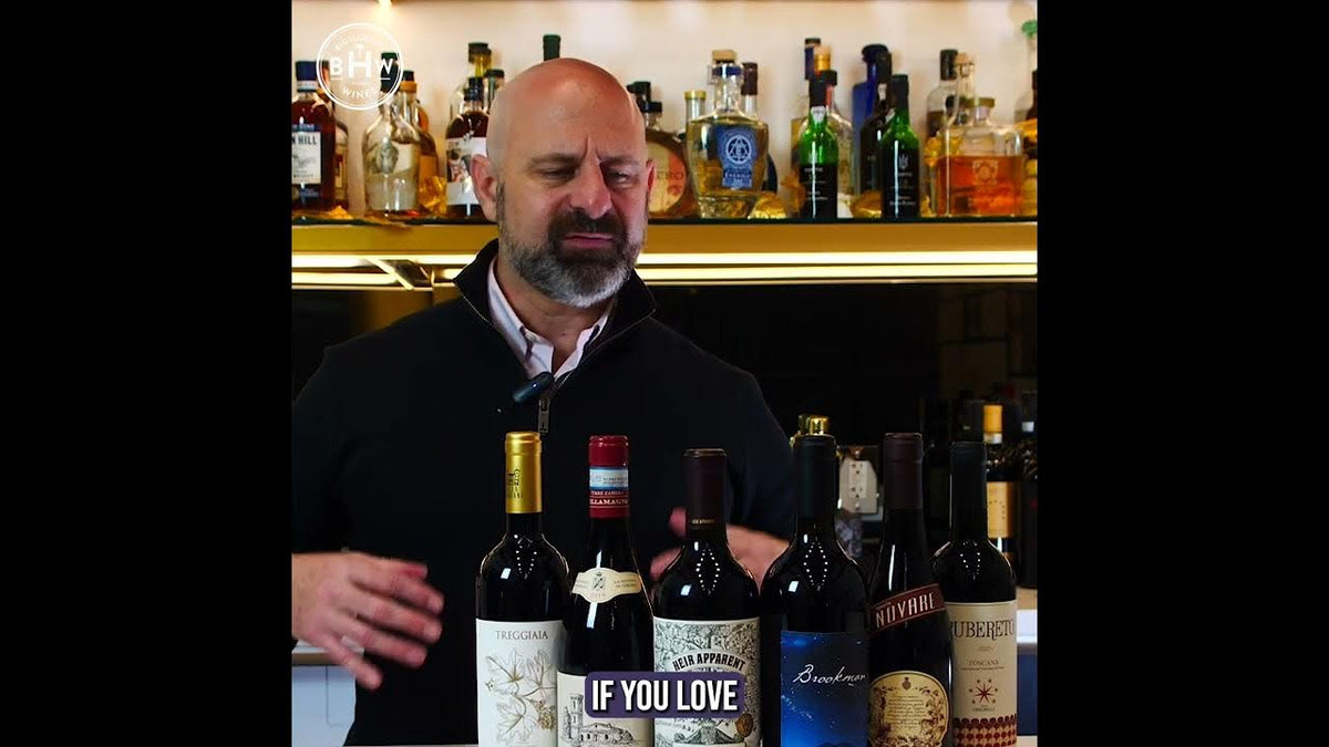 Man behind a bar gesturing toward a row of red wine bottles, caption reading "If you love"