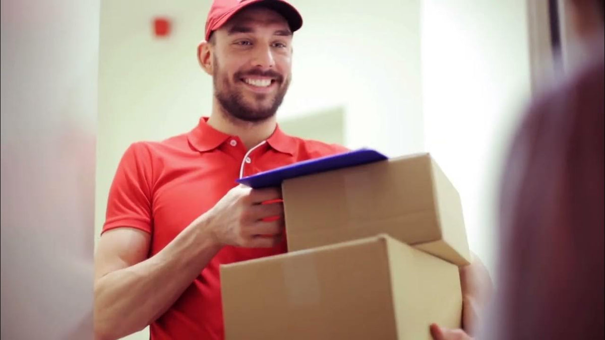 Delivery man in a red uniform and cap handing two cardboard boxes to someone at a door