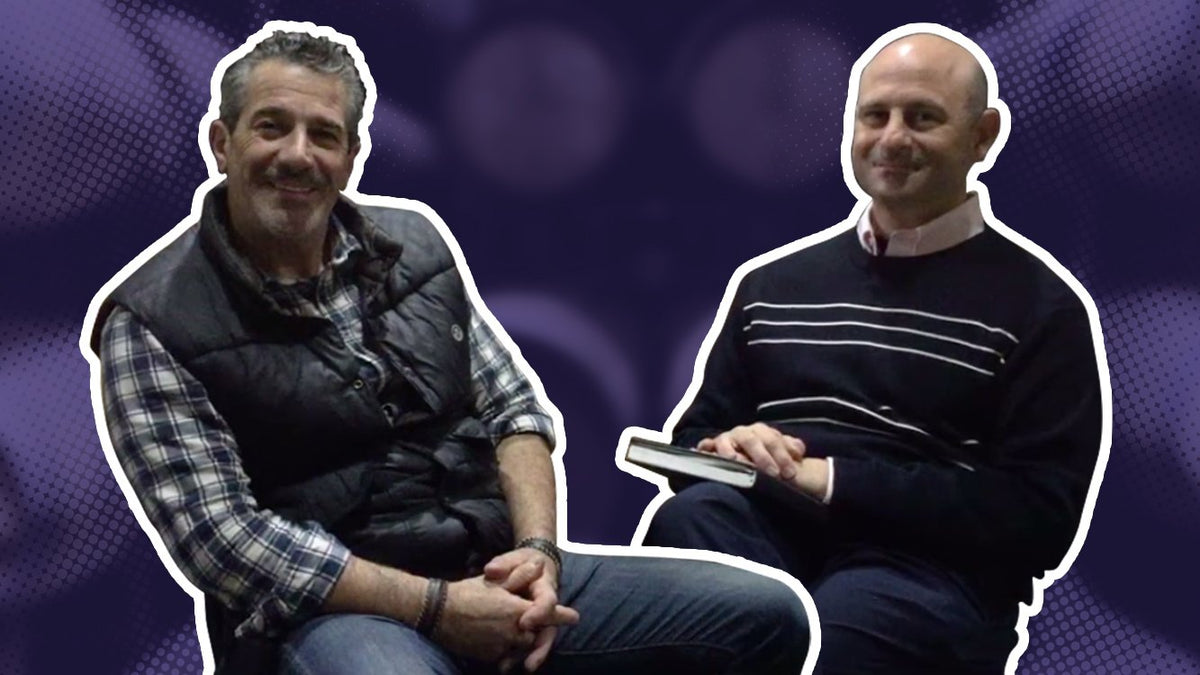 Two men seated in an interview, one holding a notepad and pen